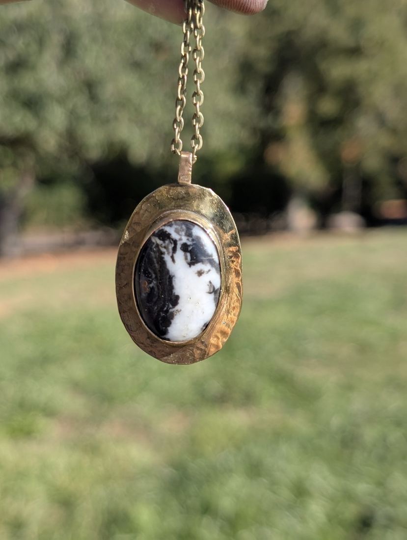 Oval black-and-white stone pendant with a wide hammered metal frame.