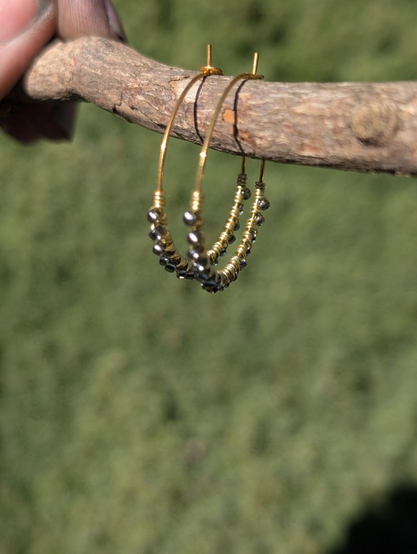Blue-gray beaded hoop earrings hanging from a branch.