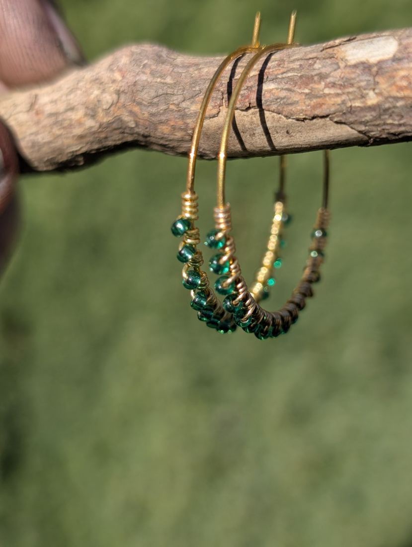 Green beaded hoop earrings hanging from a branch.