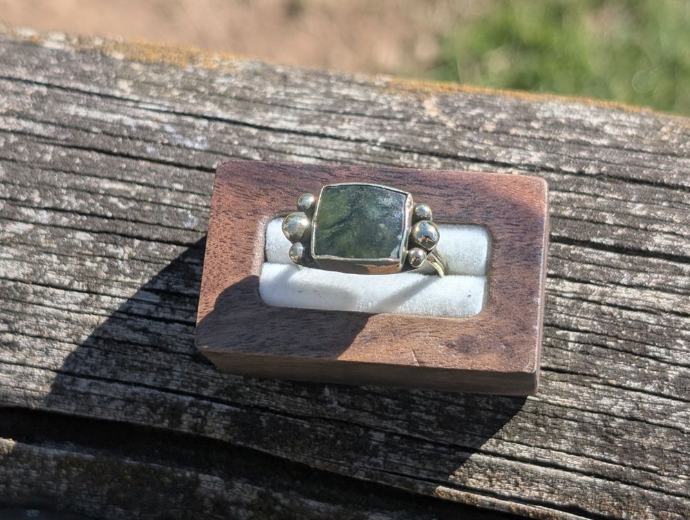 Square green stone ring with rounded metal granules along both sides, in a wooden ring box.
