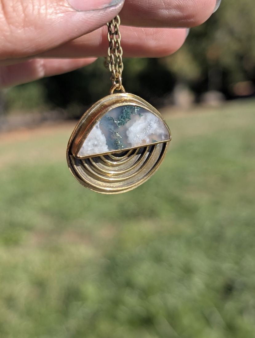 Half-moon stone pendant with green inclusions and curved metal details below.