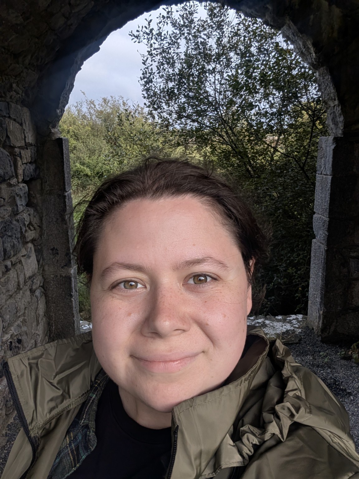 Jacquline, the maker behind The Olive Feather Co., standing beneath a stone arch outdoors.