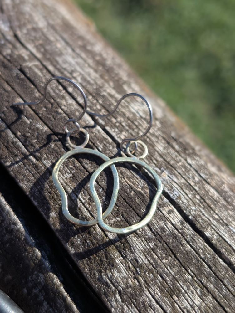 Irregular open brass loop earrings with small circular links and niobium ear hooks, resting on wood.