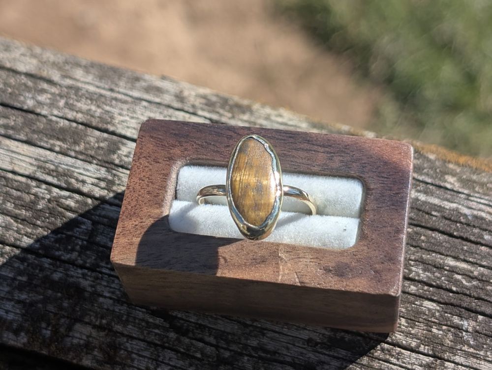 Elongated oval golden-brown stone ring displayed in a wooden ring box.