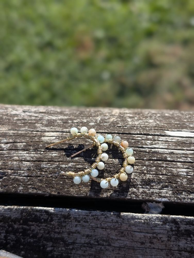 Metal hoops wrapped with pale blue, green, cream, and peach beads, resting on weathered wood.