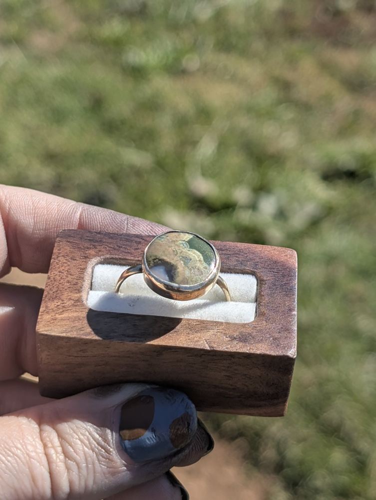Round green-and-tan patterned stone ring displayed in a wooden ring box.