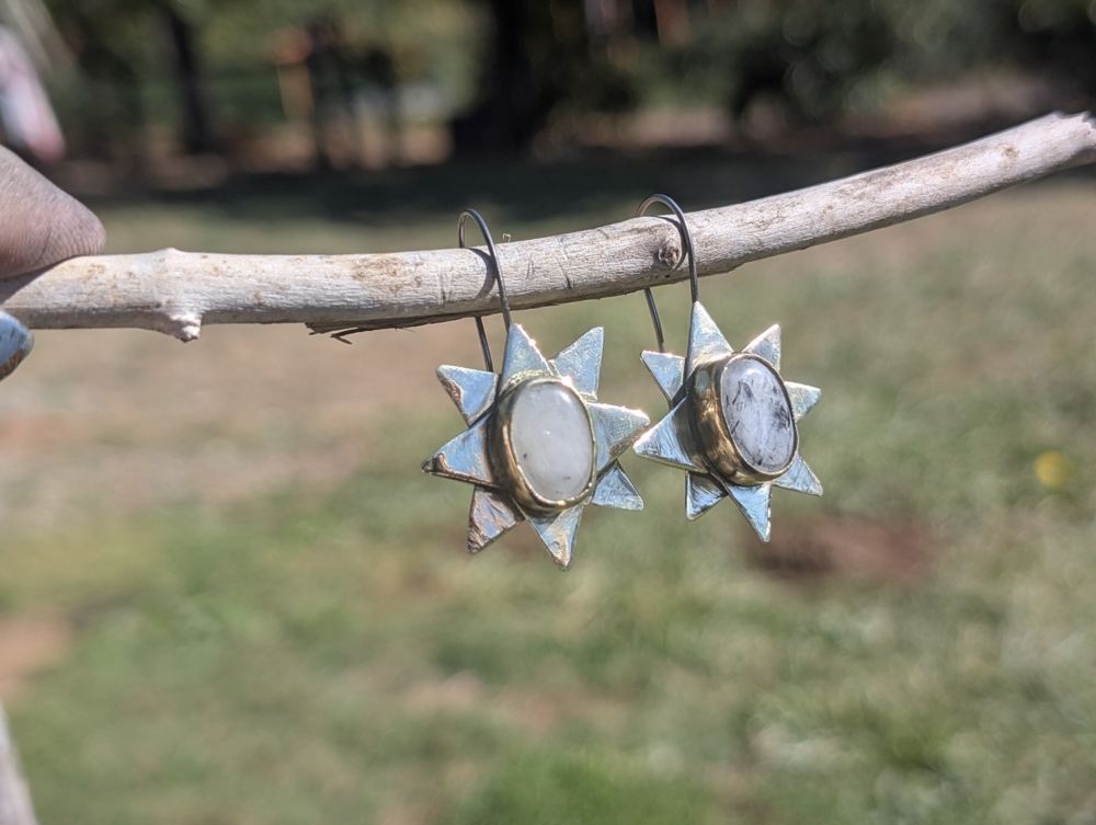 Oval pale stones in pointed starburst metal frames, hanging from a branch.