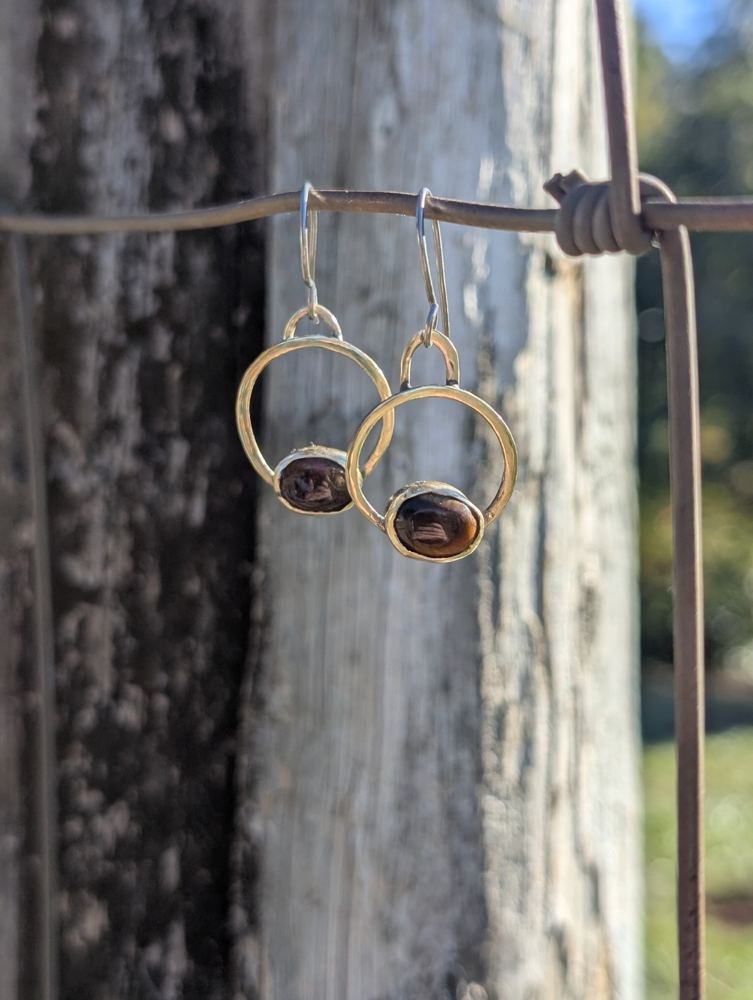 Oval brown tiger’s-eye stones set at the base of brass hoops, hanging from a wire.